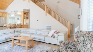 A spacious living area with a large L-shaped sofa, a wooden coffee table, and a floral armchair. A wooden staircase leads to an upper level. - Spacious cabin with game room free WIFI & parking (Shaver Lake)