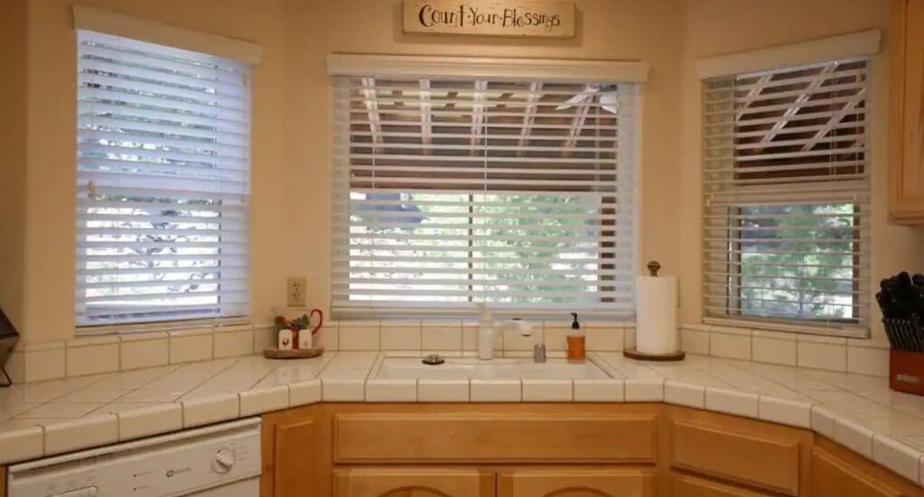 A kitchen with a built-in oven, a sink, and a window with blinds.