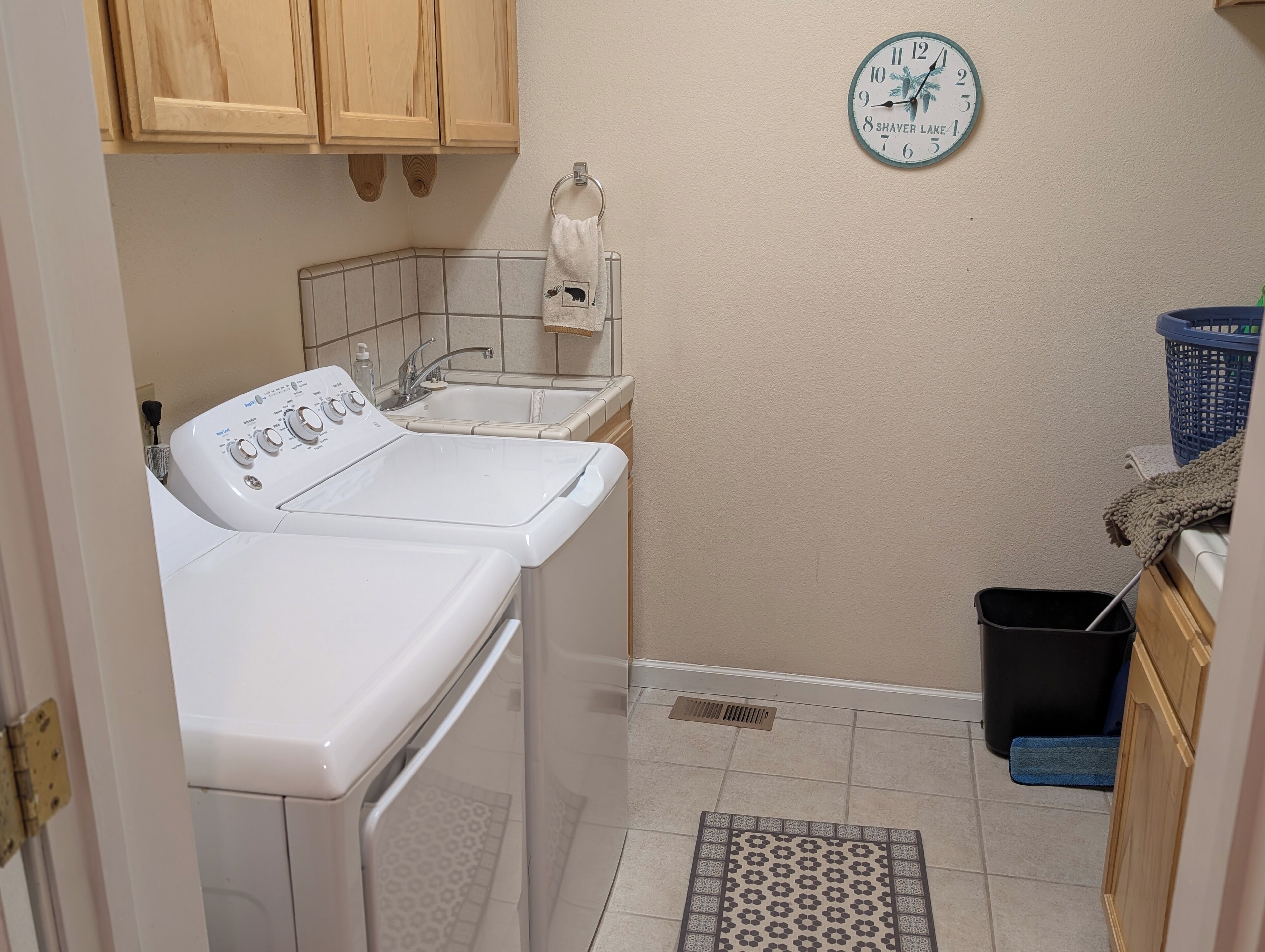 A laundry area with a washing machine, a sink, and a clock on the wall.