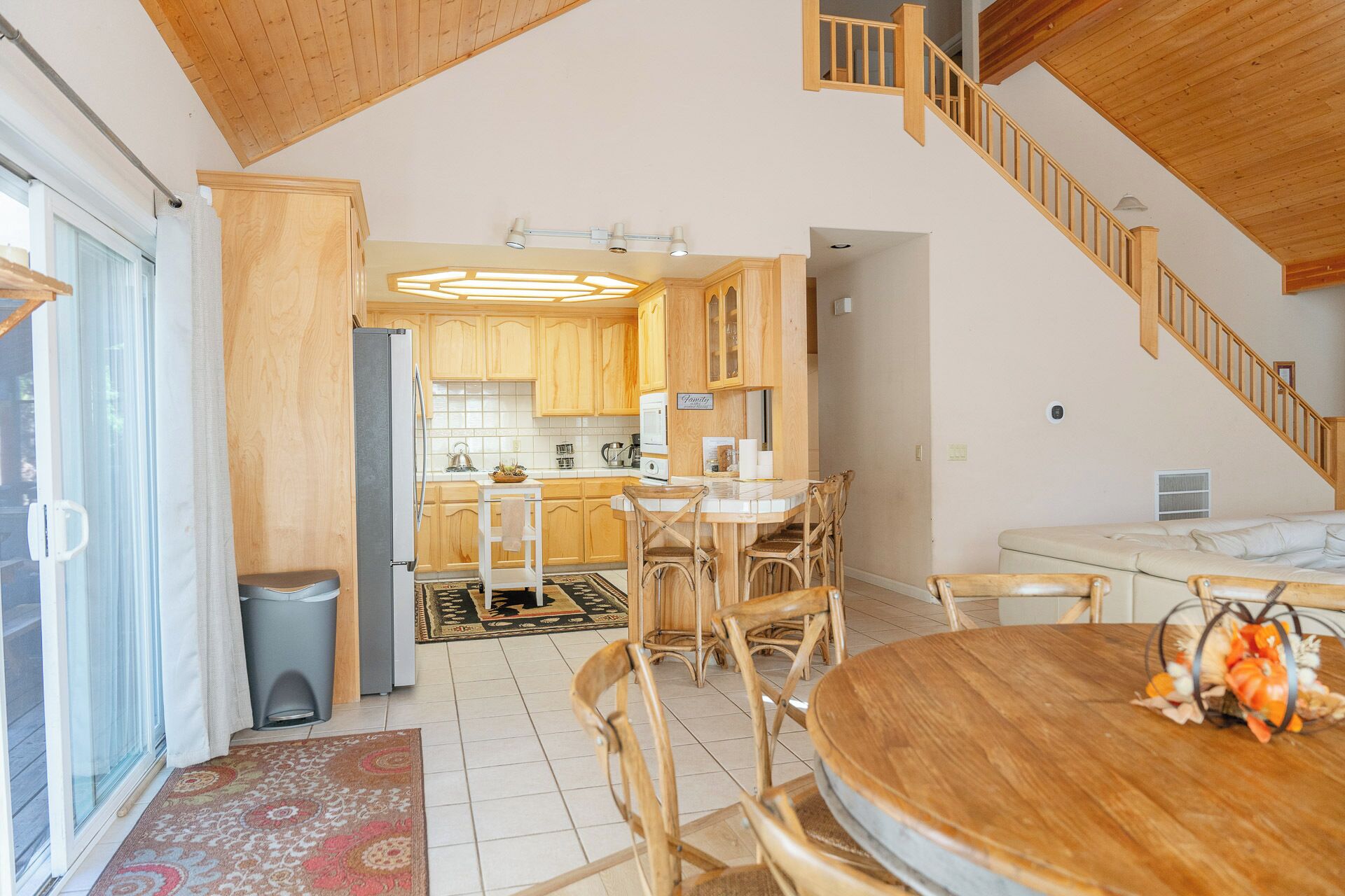 Een ruime keuken met houten kasten, een eethoek met een ronde tafel en stoelen, en een trap naar een hoger gelegen verdieping.