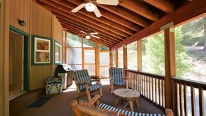 A covered porch with wooden beams, two striped chairs, a round table, and a stroller. - Spacious cabin with game room free WIFI & parking (Shaver Lake)