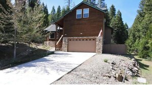A wooden cabin with a stone foundation, a garage, and a gravel driveway. - Spacious cabin with game room free WIFI & parking (Shaver Lake)
