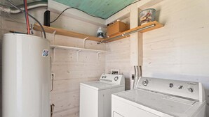 A laundry room with a white washer and dryer, wooden shelves, and a water heater. - SP615  Pet Friendly, In Town, Near Beach (Port Aransas)