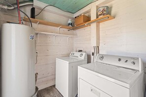 A laundry room with a white washer and dryer, wooden shelves, and a water heater. - SP615  Pet Friendly, In Town, Near Beach (Port Aransas)