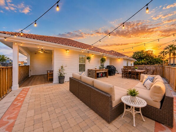 An outdoor patio with a covered seating area, a barbecue grill, and string lights.