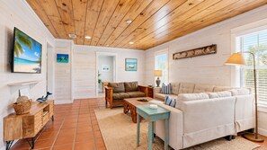 A spacious living area with a wooden ceiling, a beige sofa, a coffee table, and a television mounted on the wall.