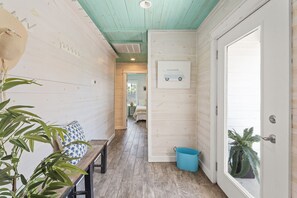 A narrow hallway with a wooden floor, a bench, a blue bucket, and a door with a window.