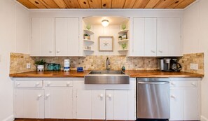 A kitchen with white cabinets, a wooden countertop, a stainless steel sink, and a dishwasher.
