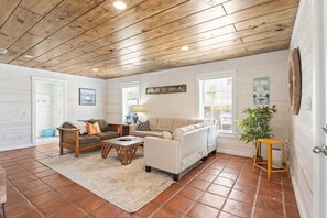 A cozy living room with a wooden ceiling, a beige sofa, a wooden coffee table, and a potted plant. - SP615  Pet Friendly, In Town, Near Beach (Port Aransas)