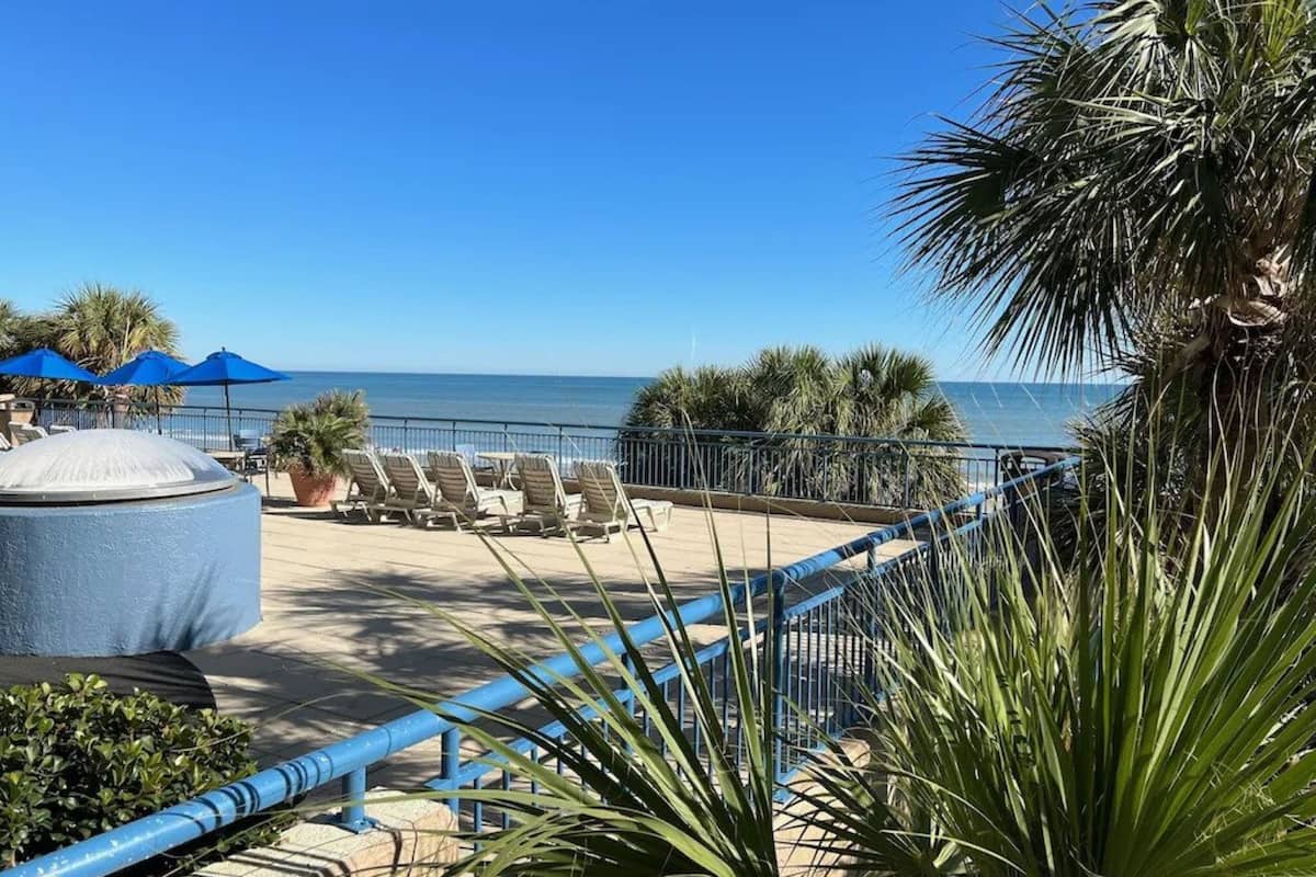 Eine Terrasse direkt am Strand mit Liegestühlen, Sonnenschirmen und einer großen Wasserspende.
