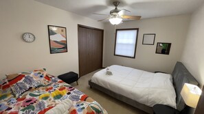 A bedroom with a bed, a chair, a ceiling fan, a clock, and a door.