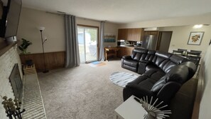 A living room with a black leather sofa, a small white table, and a kitchen area in the background.