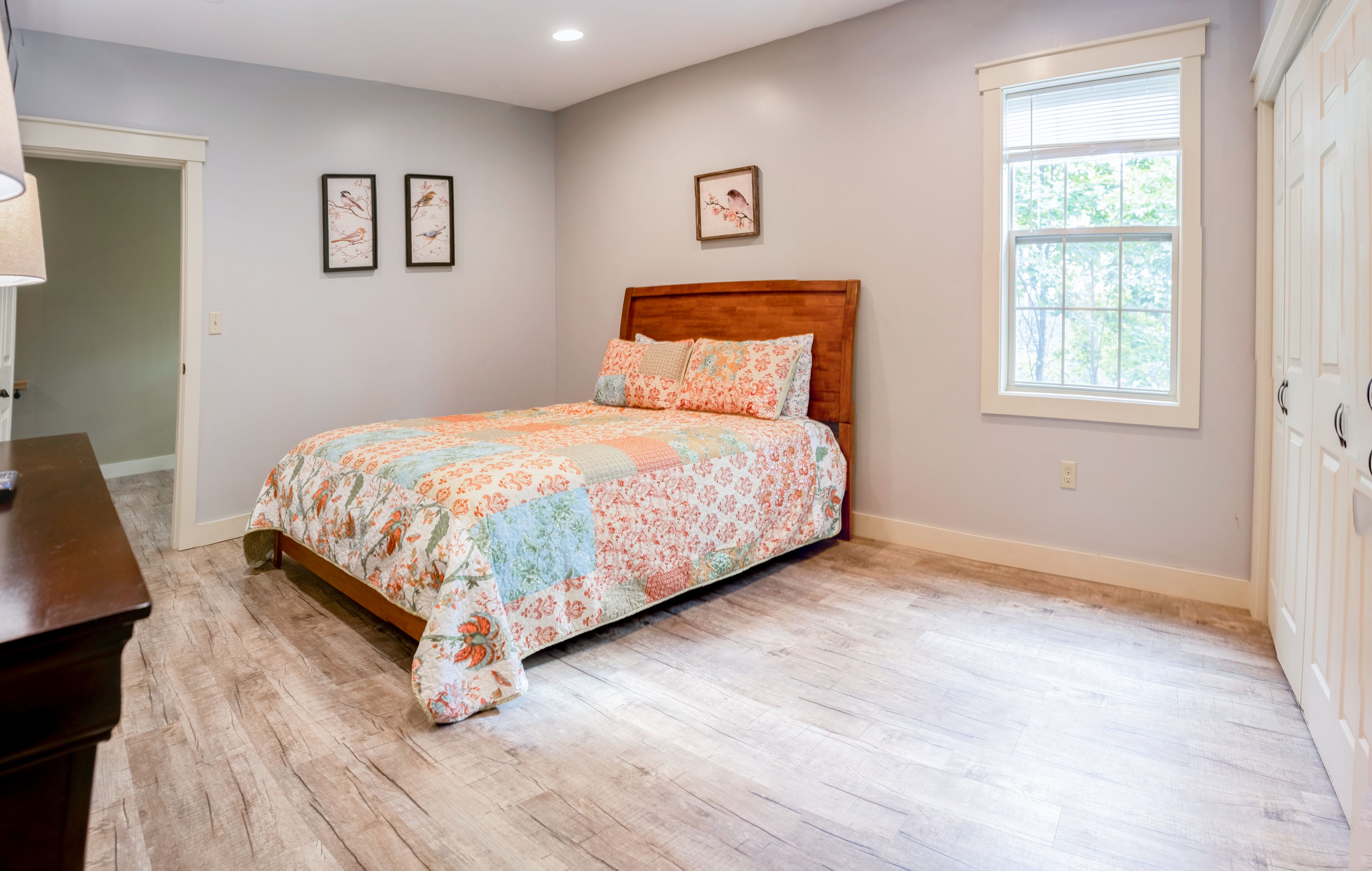 A bedroom with a wooden bed, floral bedding, a window with blinds, and a door.