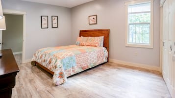 A bedroom with a wooden bed, floral bedding, a window with blinds, and a door.