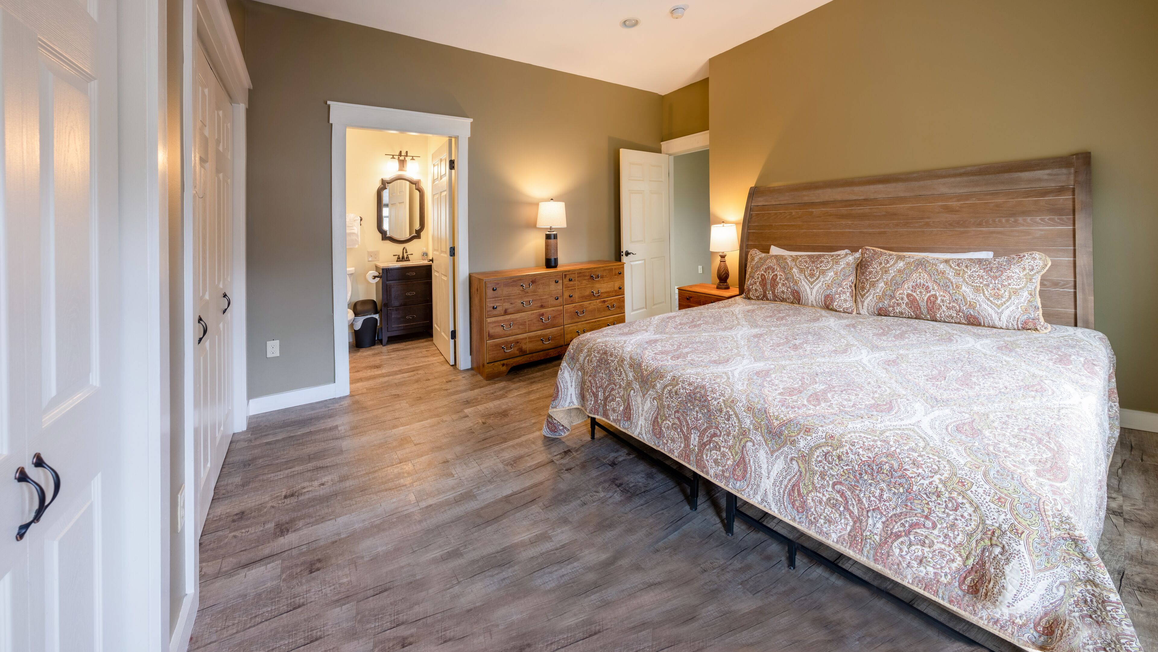 A bedroom with a large bed, wooden dresser, and a bathroom visible through an open door.