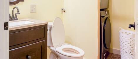 A bathroom with a wooden vanity, a white toilet, a mirror, and a laundry area.