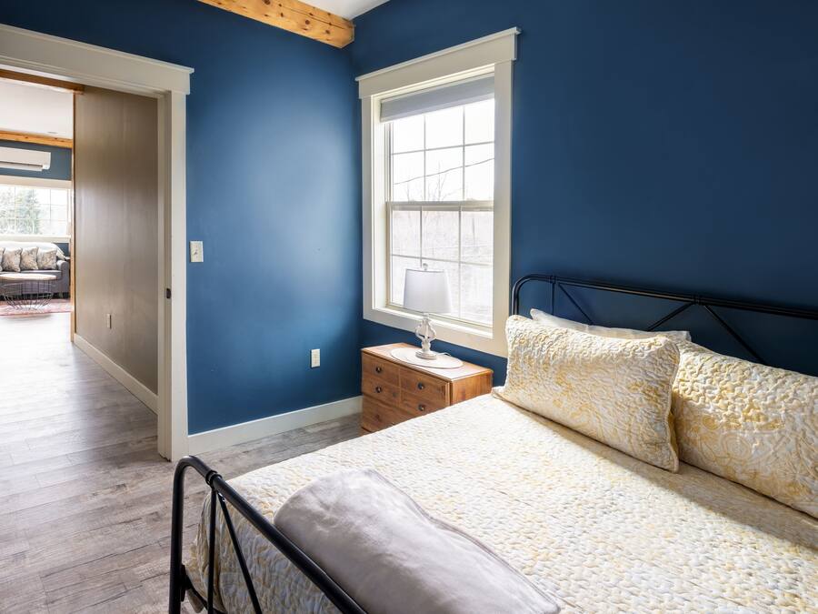Un dormitorio con cama, mesita de noche, ventana y puerta que da a otra habitación.
