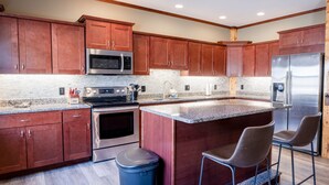Una cocina moderna con armarios de madera, electrodomésticos de acero inoxidable, encimeras de granito y una isla central con taburetes de bar.