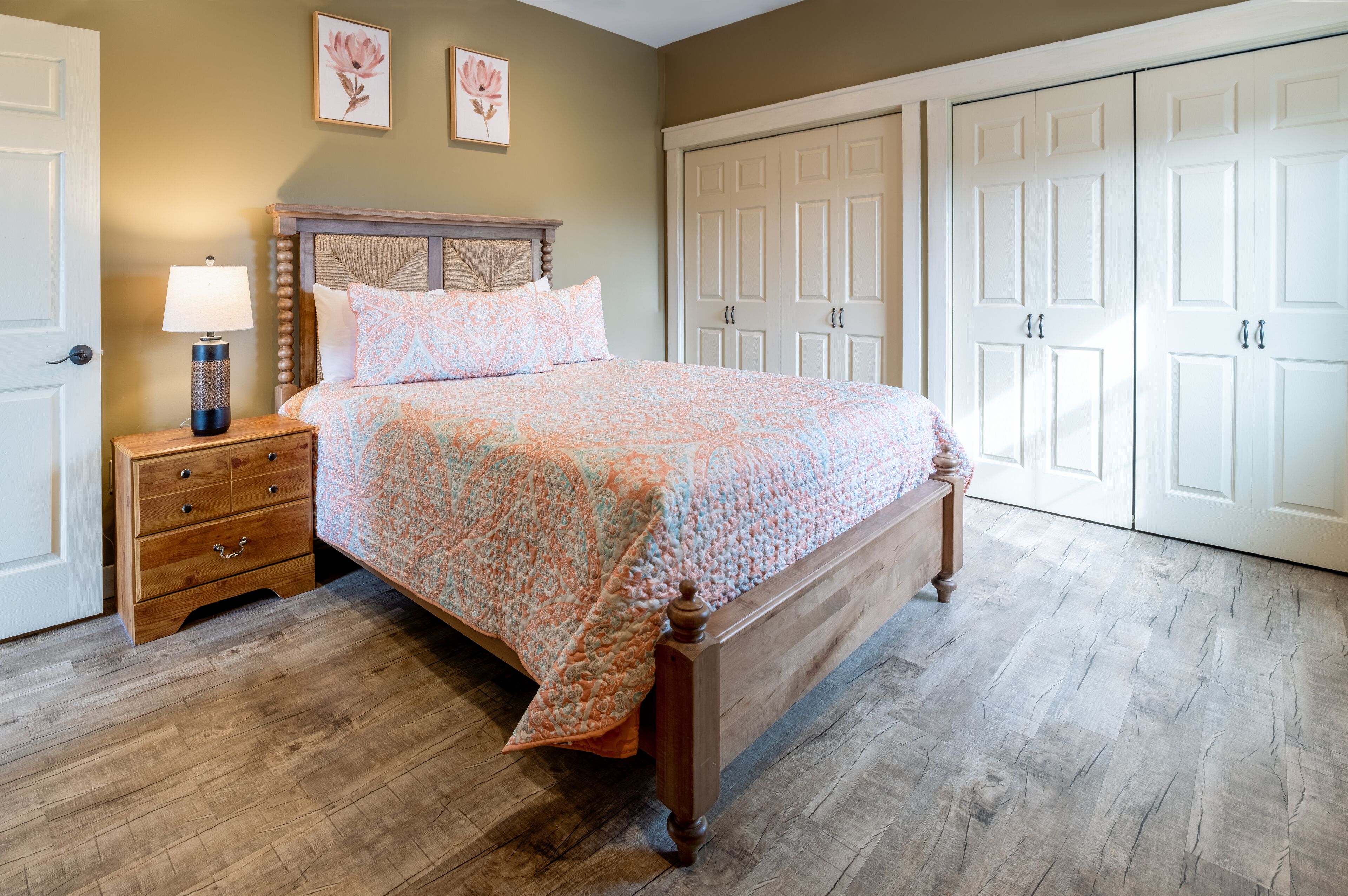 A bedroom with a wooden bed, a nightstand with a lamp, a dresser, and a wardrobe.