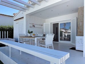 Une terrasse extérieure comprenant une table à manger, des chaises, un banc et une porte-fenêtre coulissante donnant sur une pièce adjacente.
