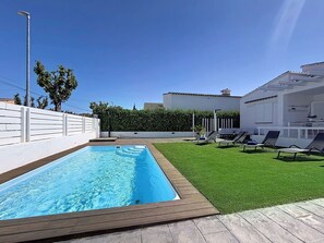 Une piscine entourée d’une terrasse en bois, d’une pelouse verdoyante et de chaises longues.