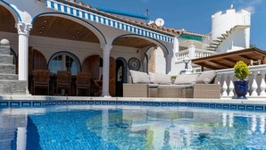 A pool area with a tiled edge, outdoor seating, and a building with arches and a clock.