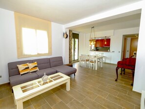 A living room with a sofa, coffee table, and a dining area with chairs and a table. - Cosy apartment for 4 guests with WIFI, A/C, pool, TV and patio (Mas Riudoms)