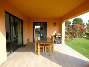 A covered patio with a dining table and chairs, a grill, and a garden view. - Cosy apartment for 4 guests with WIFI, A/C, pool, TV and patio (Mas Riudoms)