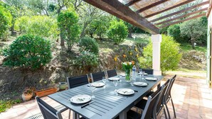 Een buitenterras met een tafel voor vier personen, omringd door stoelen, onder een houten pergola.