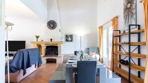 Een moderne woonkamer met een open haard, een eettafel gedekt voor vier personen en een boekenkast.