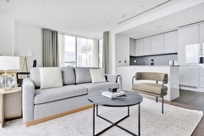 Een moderne woonkamer met een grijze bank, een ronde salontafel en een keuken met witte kasten.