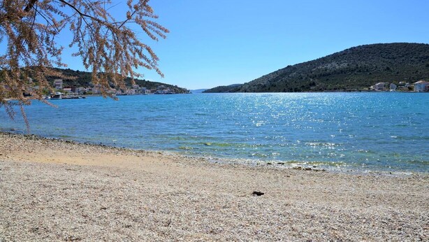 A pebble beach with clear blue water, a boat docked on the left, and hills in the background. - Lovely 2-bed Apartment in Vinisce, Close to Beach (Marina)