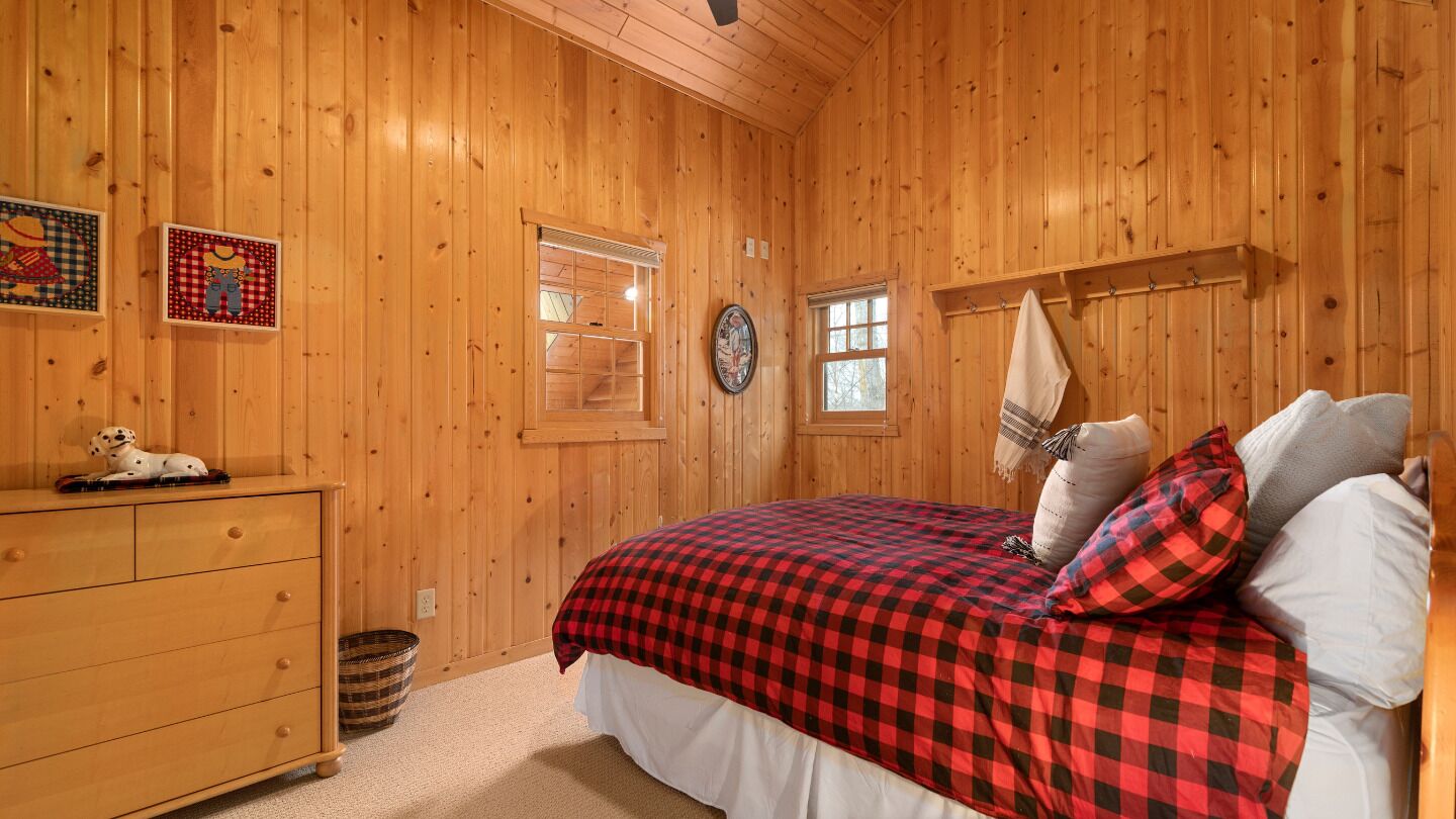 Habitación con paneles de madera, una cama, un aparador y un ventanal pequeño.