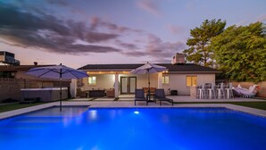 A swimming pool with two umbrellas, a patio area with chairs, and a house in the background. - 10 min to Old Town Scottsdale  (Scottsdale)