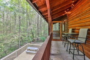Eine Holzhütte mit einer Terrasse, Sitzgelegenheiten im Freien und Blick auf einen Wald.
