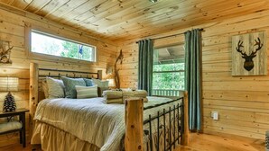 Een houten slaapkamer met een bed, gordijnen, een decoratie van een hertenkop en een raam.