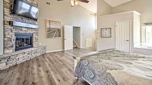 A spacious living room with a stone fireplace, a large bed, and a ceiling fan. - Boat Dock, Lake-View Decks! Ozarks Reunion Retreat (Sunrise Beach)