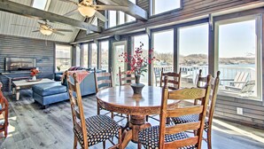 A spacious room with a large dining table, wooden chairs, and a view of the water. - Boat Dock, Lake-View Decks! Ozarks Reunion Retreat (Sunrise Beach)