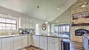A spacious kitchen with white cabinets, a stone fireplace, and a dining area with a view. - Boat Dock, Lake-View Decks! Ozarks Reunion Retreat (Sunrise Beach)