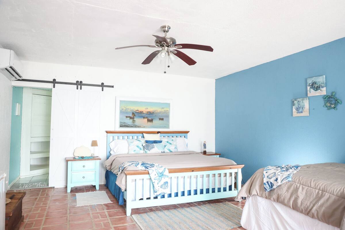 Un dormitorio con cama, mesita de noche, ventilador de techo y un cuadro en la pared.