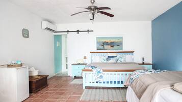 Une chambre à coucher comprenant un lit, un ventilateur de plafond, un climatiseur, une table de chevet, une commode et une fenêtre avec un tableau.