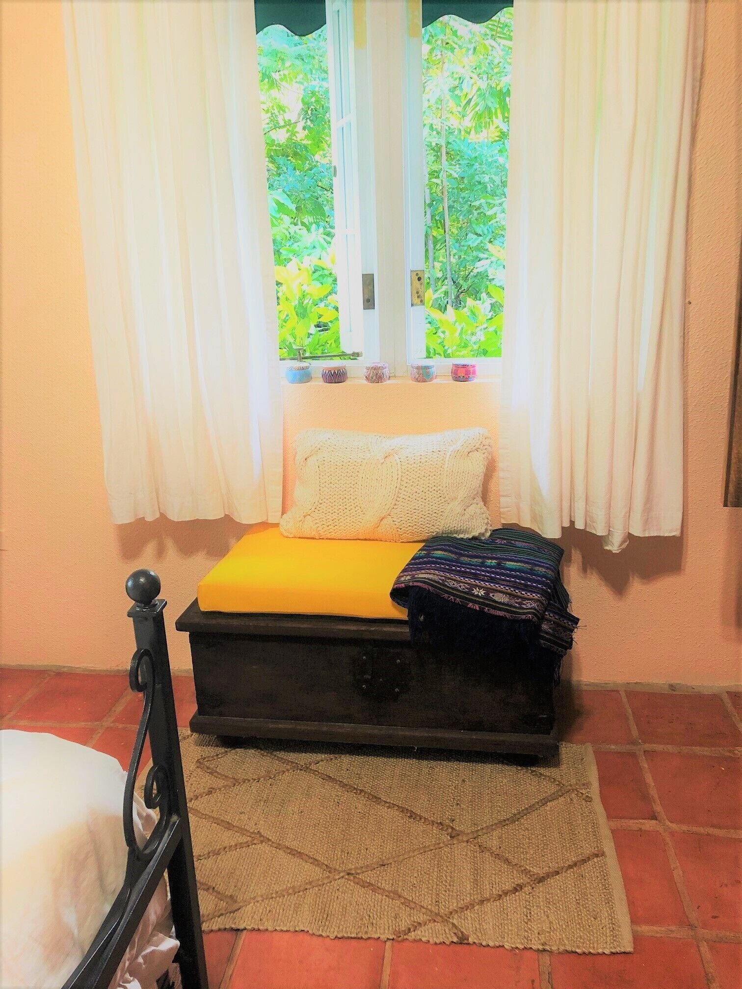 A small bedroom with a bed, a window with curtains, and a view of greenery outside.