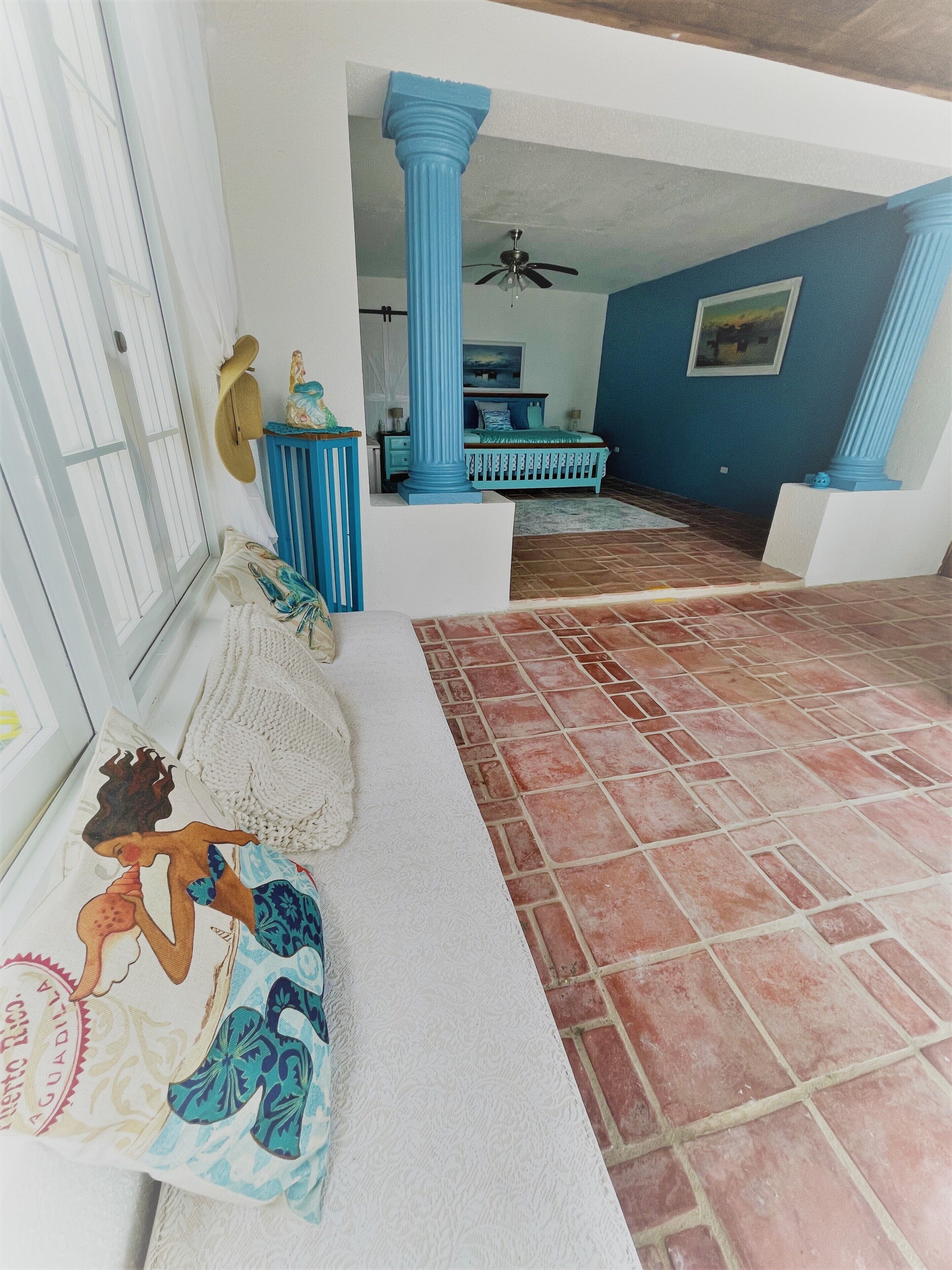 A room with a white bench, a blue column, and a tiled floor.