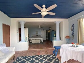 A room with a ceiling fan, a bed, a table with a tablecloth, and a patterned rug.