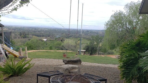 Une terrasse dotée d’un foyer circulaire entouré de chaises en métal, d’une balançoire et offrant une vue sur un paysage rural.