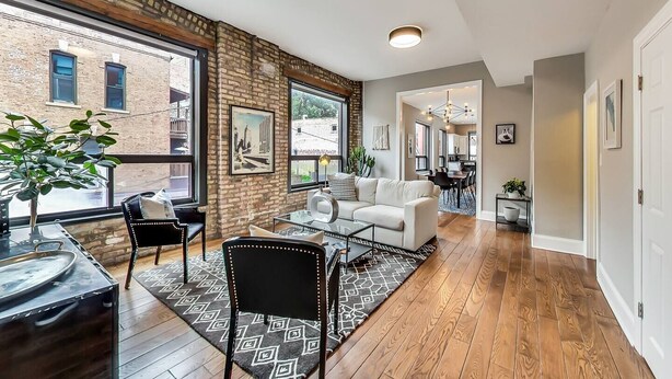 A spacious living area with a brick wall, large windows, a white sofa, and a dining table. - Lovely 4 Bedroom Spot located in Charming Old Town (Chicago)