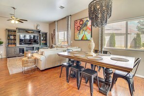 A spacious living room with a dining area, a ceiling fan, a large painting, and a view of the outdoors.