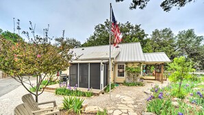 Een klein huis met een metalen dak, een vlaggenmast met een Amerikaanse vlag, een tuin vol paarse bloemen en een houten terras.