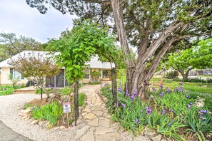 Ein Steinweg führt zu einem Haus mit einer Veranda, umgeben von einem Garten mit violetten Blumen und einem Warnschild.