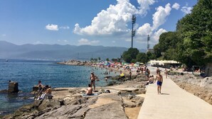 Rantaviiva, jossa on kivikkoista maastoa, betoninen kävelyreitti ja kirkas, sininen taivas.
